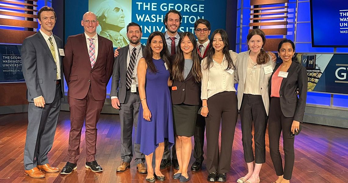 Group photo of residents on a TV set with George Washington University Logo on a screen in the background